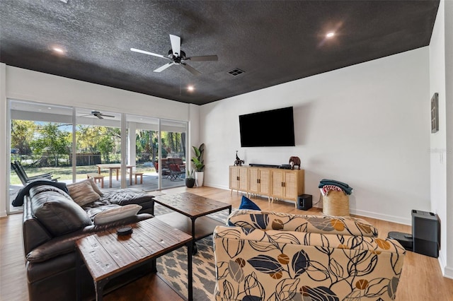 living area with a textured ceiling, wood finished floors, visible vents, baseboards, and a ceiling fan