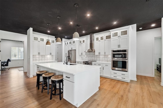 kitchen with stainless steel appliances, a spacious island, light countertops, a sink, and wall chimney range hood