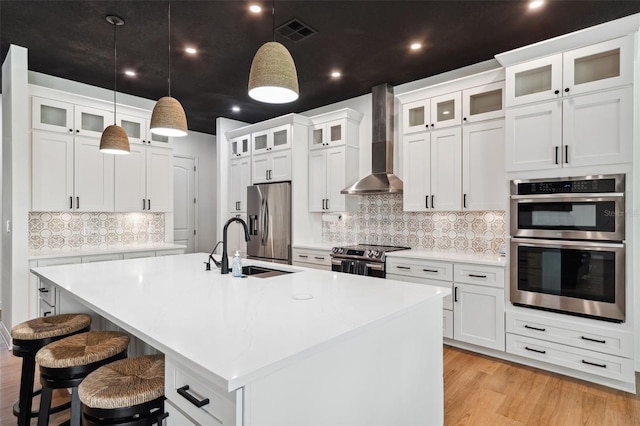 kitchen featuring a sink, visible vents, appliances with stainless steel finishes, wall chimney exhaust hood, and a center island with sink