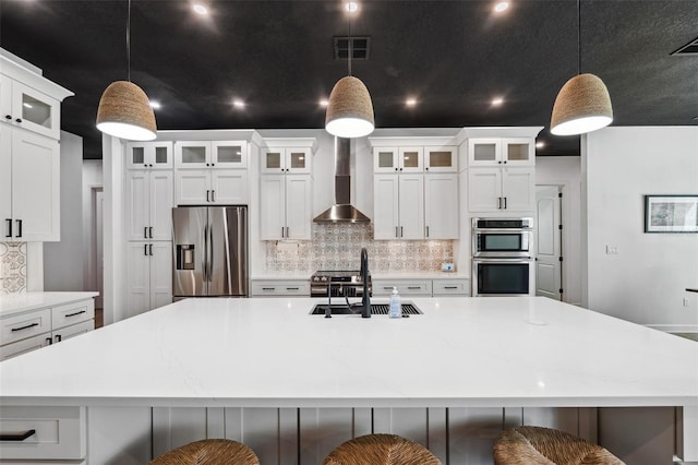 kitchen featuring a spacious island, a sink, visible vents, appliances with stainless steel finishes, and wall chimney range hood