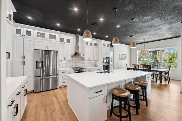 kitchen featuring stainless steel appliances, a sink, visible vents, wall chimney range hood, and a center island with sink