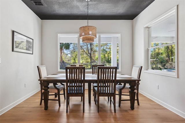 dining space with baseboards, a textured ceiling, visible vents, and wood finished floors