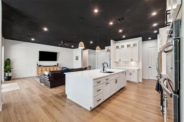 kitchen featuring a sink, open floor plan, light countertops, light wood finished floors, and a center island with sink