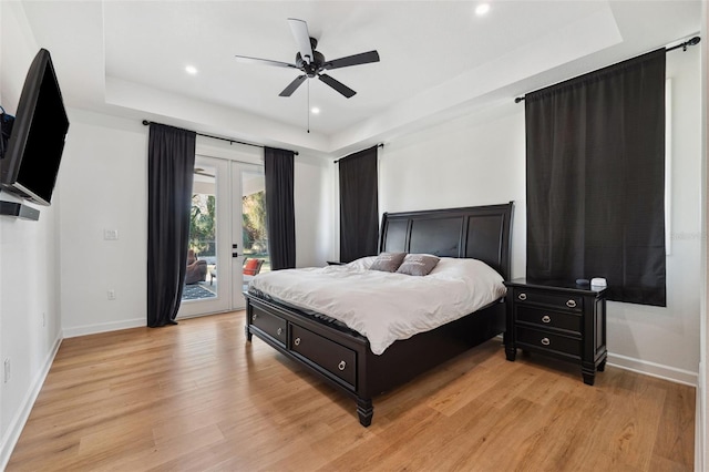 bedroom featuring baseboards, light wood-style floors, access to exterior, french doors, and a raised ceiling