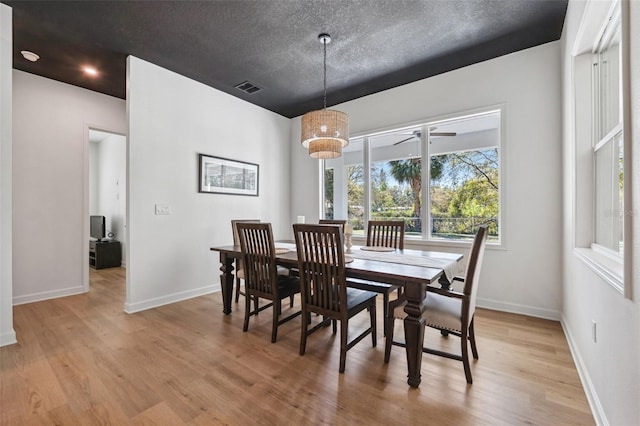 dining area featuring a textured ceiling, baseboards, visible vents, and light wood-style floors