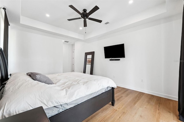 bedroom featuring a tray ceiling, recessed lighting, ceiling fan, light wood-type flooring, and baseboards