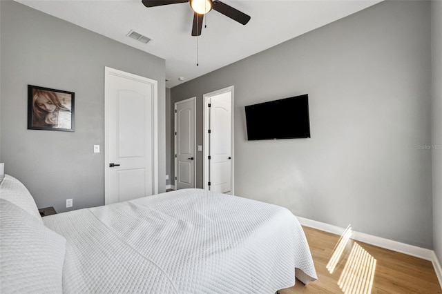 bedroom with a ceiling fan, wood finished floors, visible vents, and baseboards