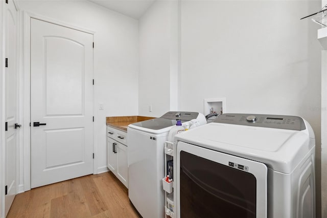 laundry room with separate washer and dryer, light wood-type flooring, and cabinet space