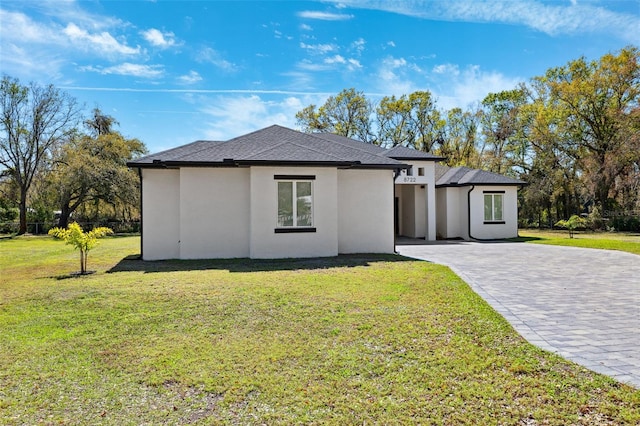 prairie-style home with a shingled roof, decorative driveway, a front yard, and stucco siding