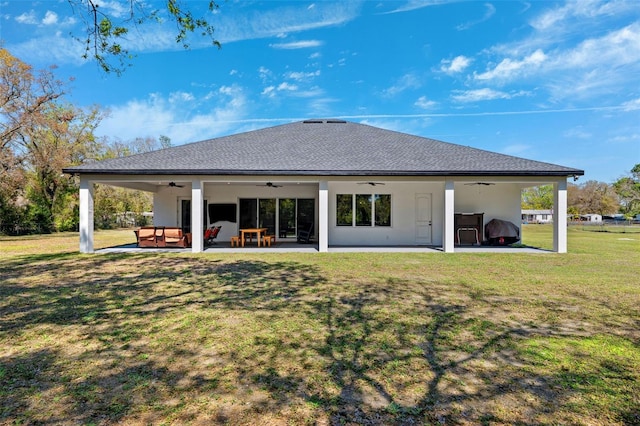 back of property with ceiling fan, a patio, a shingled roof, and a lawn