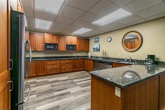634 Edgewater Dr Unit 744, Dunedin, FL 34698 - kitchen with stainless steel appliances, brown cabinetry, a peninsula, dark stone counters, and light wood-style floors