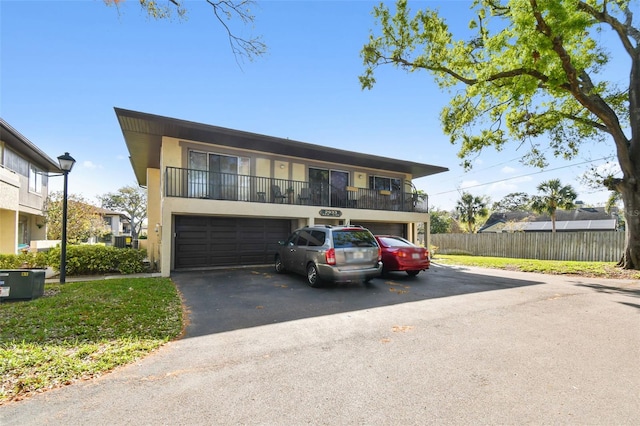 multi unit property with a balcony, a garage, fence, driveway, and stucco siding