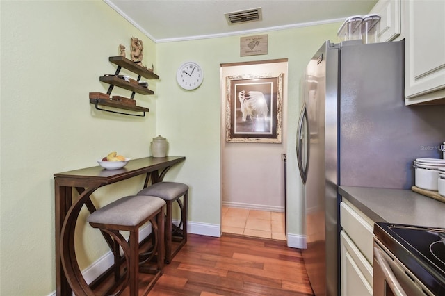 kitchen with dark wood-type flooring, visible vents, baseboards, white cabinets, and freestanding refrigerator