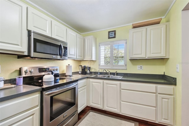 kitchen with appliances with stainless steel finishes, dark countertops, white cabinets, and a sink