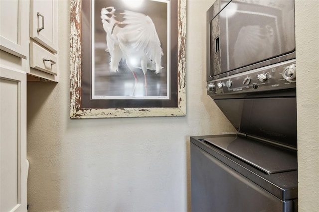 laundry area featuring cabinet space, stacked washer and dryer, and a textured wall