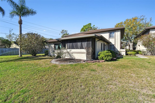 rear view of house featuring fence, a lawn, and stucco siding