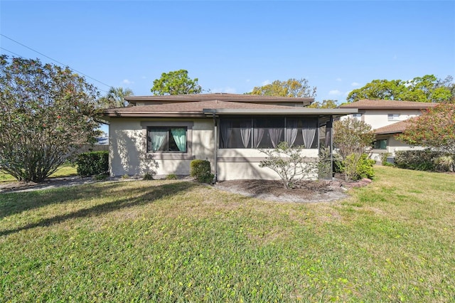 back of property featuring a sunroom, a yard, and stucco siding