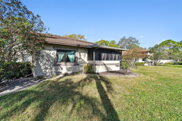 rear view of house featuring a sunroom, a lawn, and stucco siding