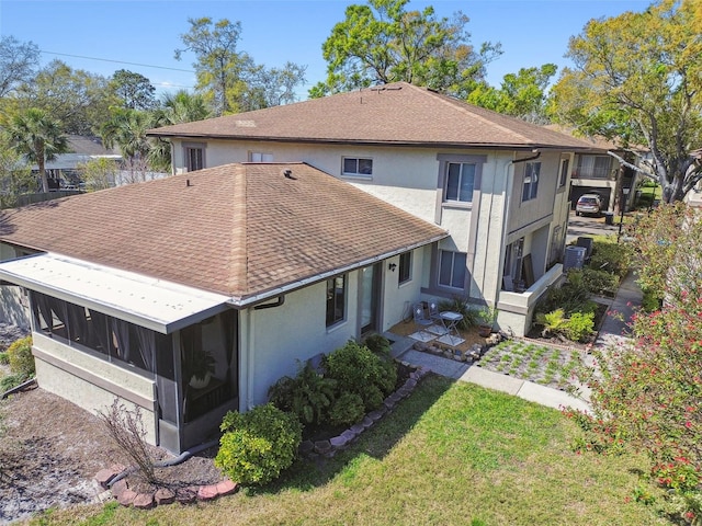 rear view of property with a sunroom, a shingled roof, a lawn, and stucco siding