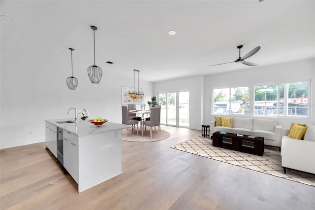 kitchen featuring hanging light fixtures, light wood-style flooring, open floor plan, and a sink