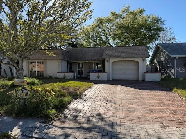 ranch-style home with decorative driveway, an attached garage, roof with shingles, and stucco siding