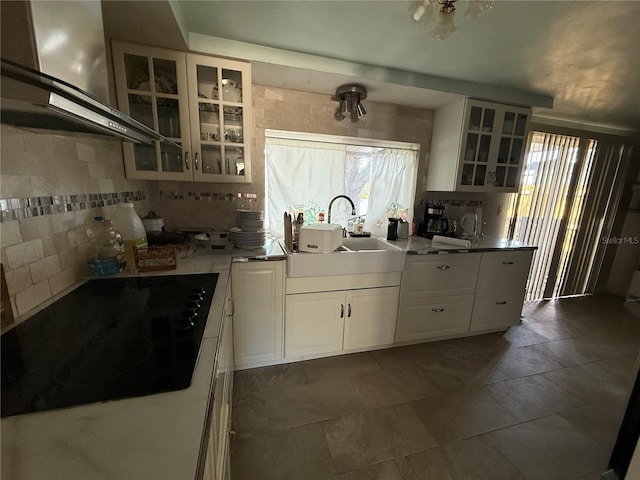 kitchen with glass insert cabinets, range hood, white cabinets, black electric cooktop, and a sink