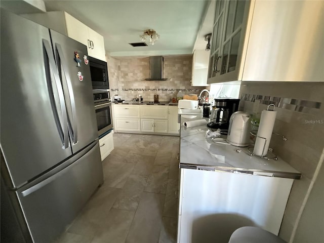 kitchen with backsplash, white cabinets, black appliances, wall chimney exhaust hood, and a sink