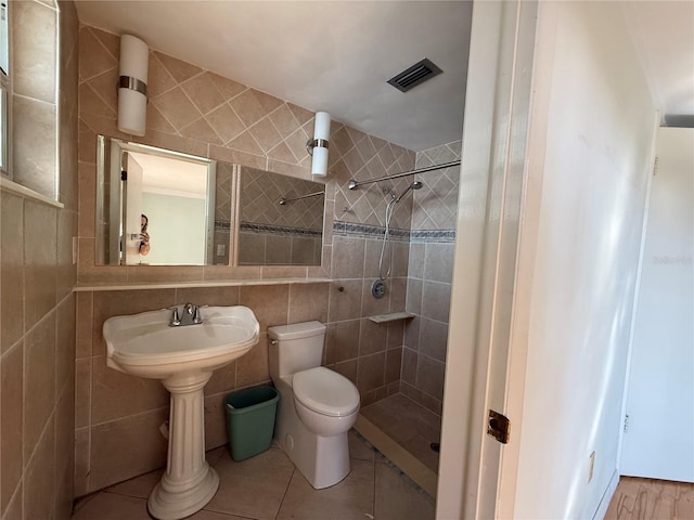 bathroom with visible vents, toilet, tile walls, and a tile shower