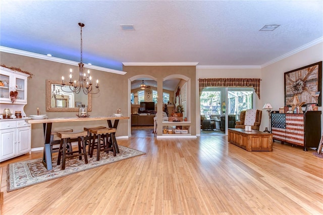 dining space featuring arched walkways, a textured ceiling, light wood-style flooring, ceiling fan with notable chandelier, and ornamental molding