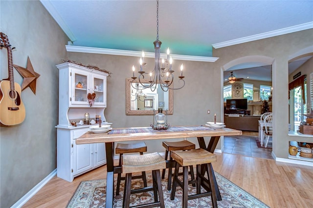 dining area with arched walkways, crown molding, light wood-type flooring, baseboards, and ceiling fan with notable chandelier