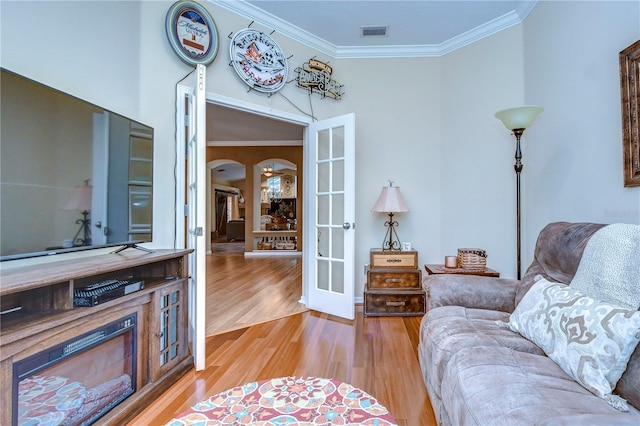 living room with arched walkways, ornamental molding, light wood-style flooring, and visible vents