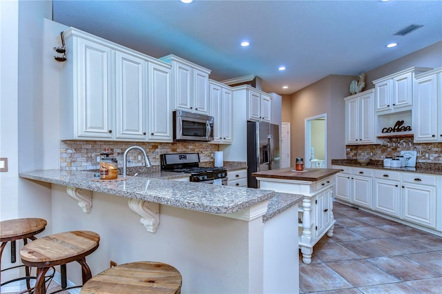 kitchen featuring decorative backsplash, a breakfast bar area, appliances with stainless steel finishes, a peninsula, and open shelves