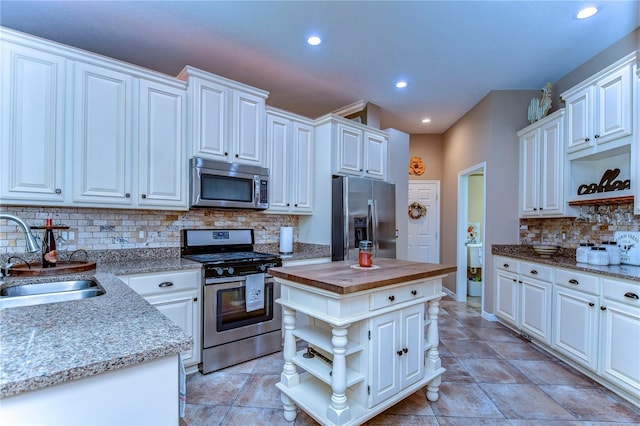 kitchen featuring white cabinets, butcher block counters, appliances with stainless steel finishes, open shelves, and a sink