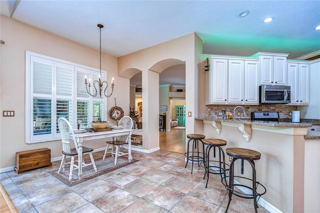 kitchen featuring light stone counters, a breakfast bar, white cabinets, decorative backsplash, and stainless steel microwave