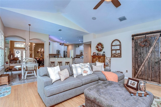 living room featuring vaulted ceiling, a barn door, visible vents, and light wood-style floors