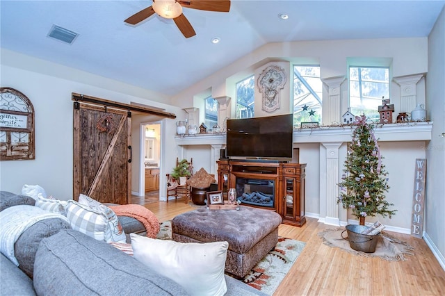 living area with vaulted ceiling, a barn door, wood finished floors, and visible vents