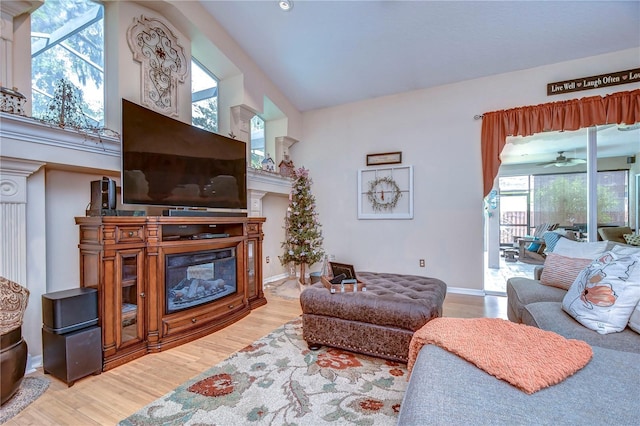 living room with baseboards, ceiling fan, a glass covered fireplace, and light wood-style floors