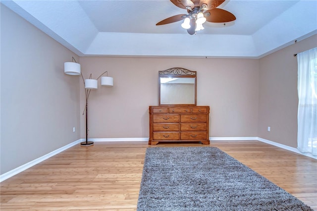 unfurnished bedroom with ceiling fan, a tray ceiling, light wood-style flooring, and baseboards