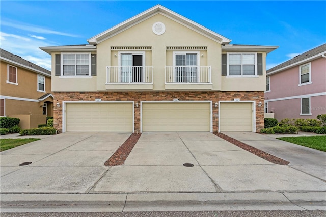 townhome / multi-family property featuring an attached garage, stone siding, driveway, and stucco siding