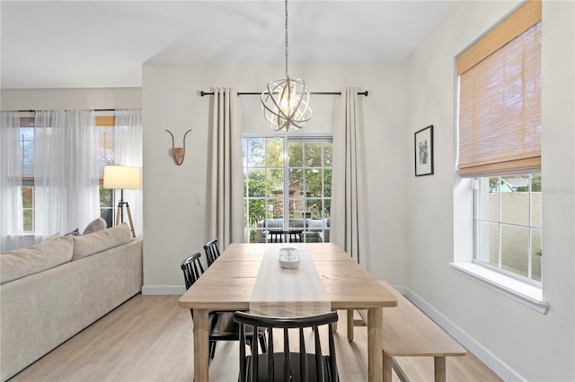 dining area featuring light wood-type flooring, a wealth of natural light, baseboards, and a notable chandelier