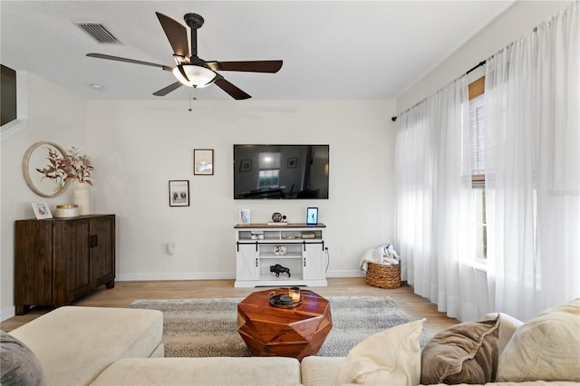 living room with light wood-style flooring, a ceiling fan, visible vents, and baseboards