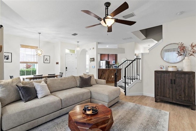 living room with stairway, light wood-type flooring, visible vents, and arched walkways