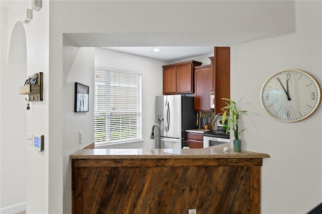 kitchen with a peninsula, light stone counters, stainless steel appliances, and recessed lighting