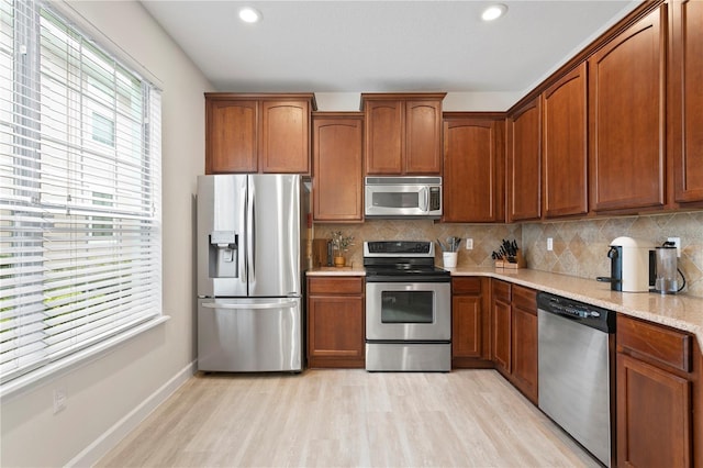 kitchen with stainless steel appliances, brown cabinets, light wood-style flooring, and decorative backsplash