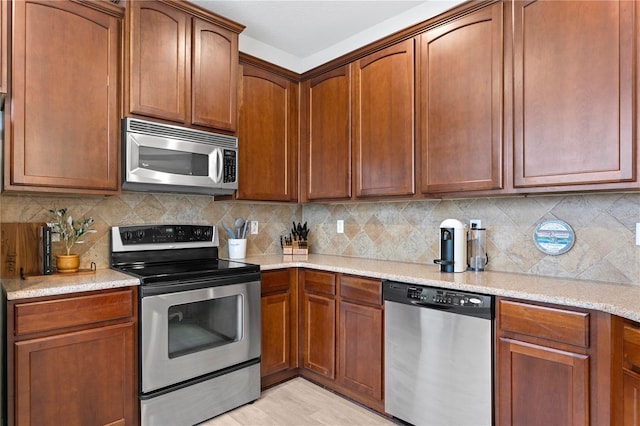 kitchen with light wood finished floors, tasteful backsplash, brown cabinetry, light stone countertops, and stainless steel appliances