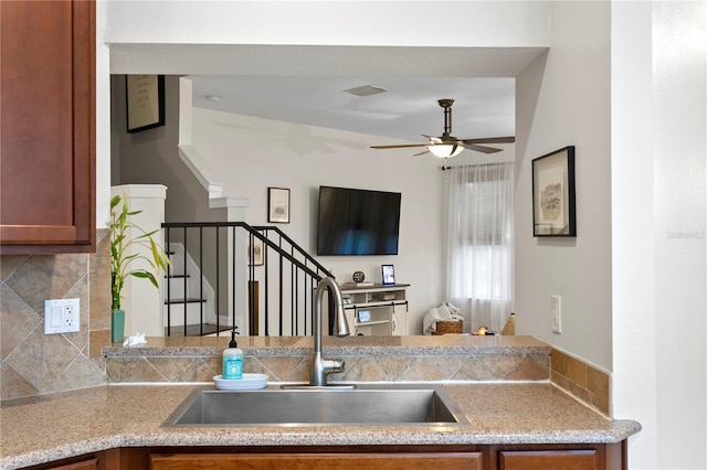 kitchen with visible vents, brown cabinetry, ceiling fan, a sink, and backsplash