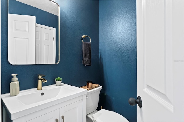 bathroom with toilet, a textured wall, and vanity