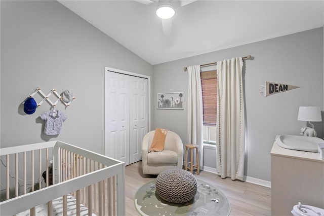 bedroom featuring ceiling fan, light wood-style floors, vaulted ceiling, a closet, and a nursery area