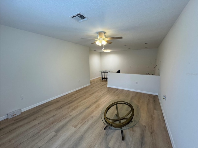 unfurnished room with visible vents, light wood-style flooring, a ceiling fan, a textured ceiling, and baseboards