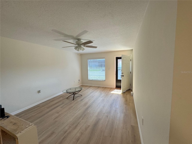 empty room with a textured ceiling, ceiling fan, light wood-type flooring, and baseboards